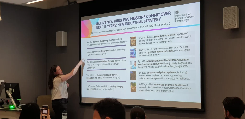 A speaker presents a slide on the UK’s five quantum research hubs and missions at the Quantum × Society Research Sandpit